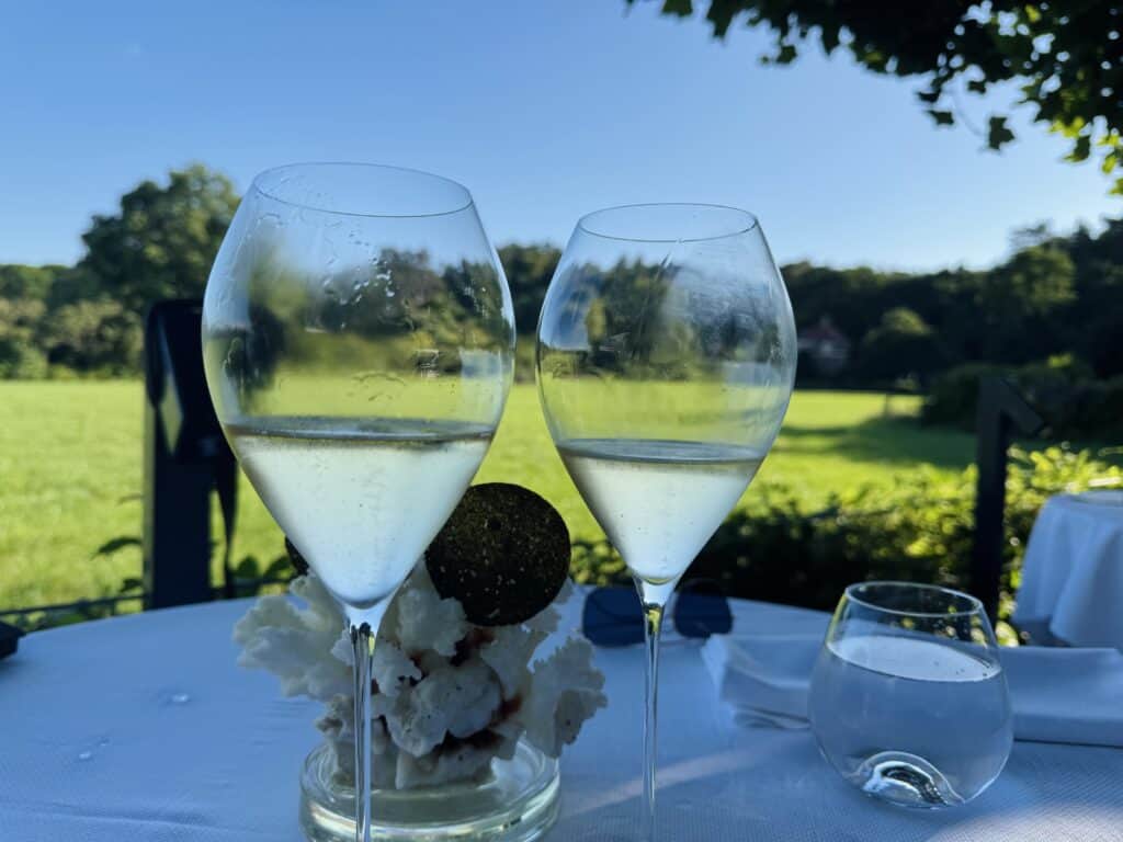 Twee glazen champagne op het terras van Merlet met uitzicht op een weiland
