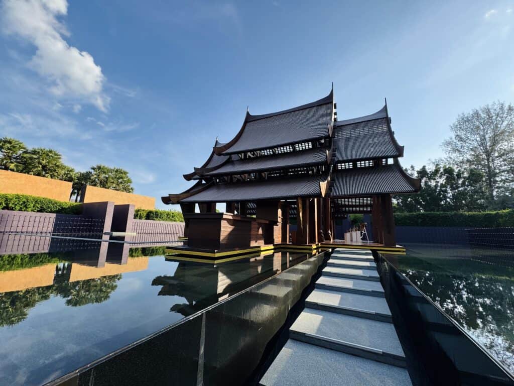 A traditional Thai pavilion at Phulay Bay, a Ritz-Carlton Reserve, nestled in a reflecting lotus pond in Krabi. An iconic wooden pavilion at Phulay Bay, a Ritz-Carlton Reserve in Krabi, surrounded by a serene lotus pond. The architecture reflects traditional Lanna design with graceful roofs and tranquil water reflections, a signature element of this exclusive luxury resort. 