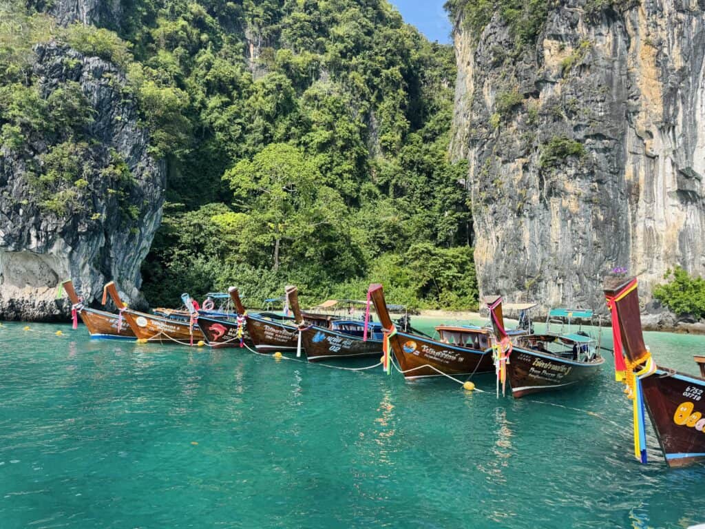 Colorful longtail boats moored in the turquoise waters of Hong Island, surrounded by towering limestone rock formations.